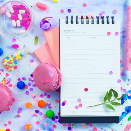 Party management and organization concept with sweets, confetti and an open notepad with blank pages