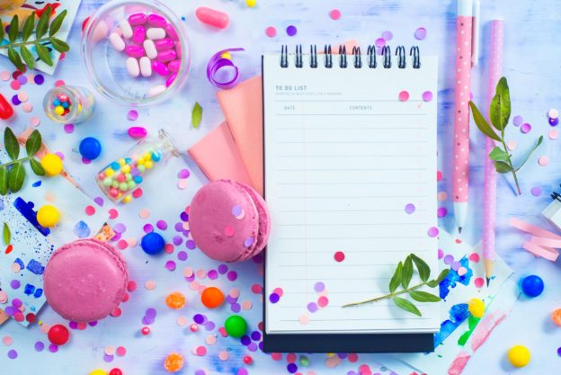 Party management and organization concept with sweets, confetti and an open notepad with blank pages